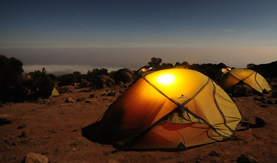 Small tent pitched on a rocky campsite at dusk with multiple tents